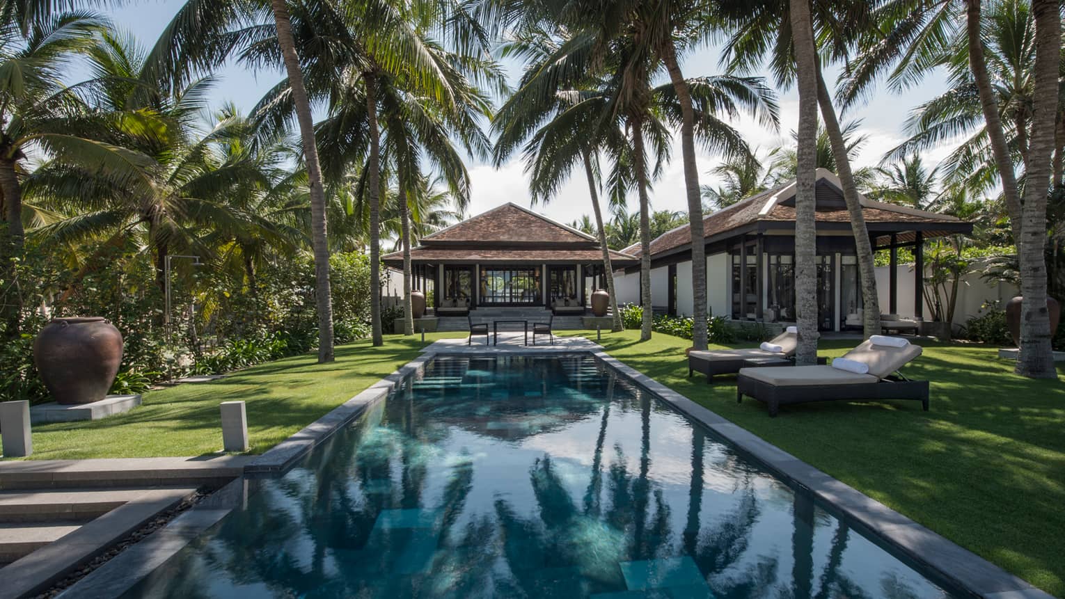 Pool villa, small patio table at end of outdoor swimming pool under palms