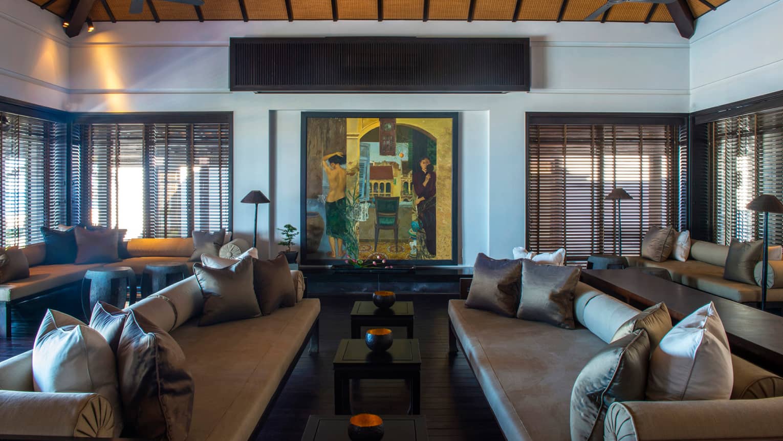 Large colourful oil painting on wall over two sofas, tables with brass bowls, under soaring wood ceilings