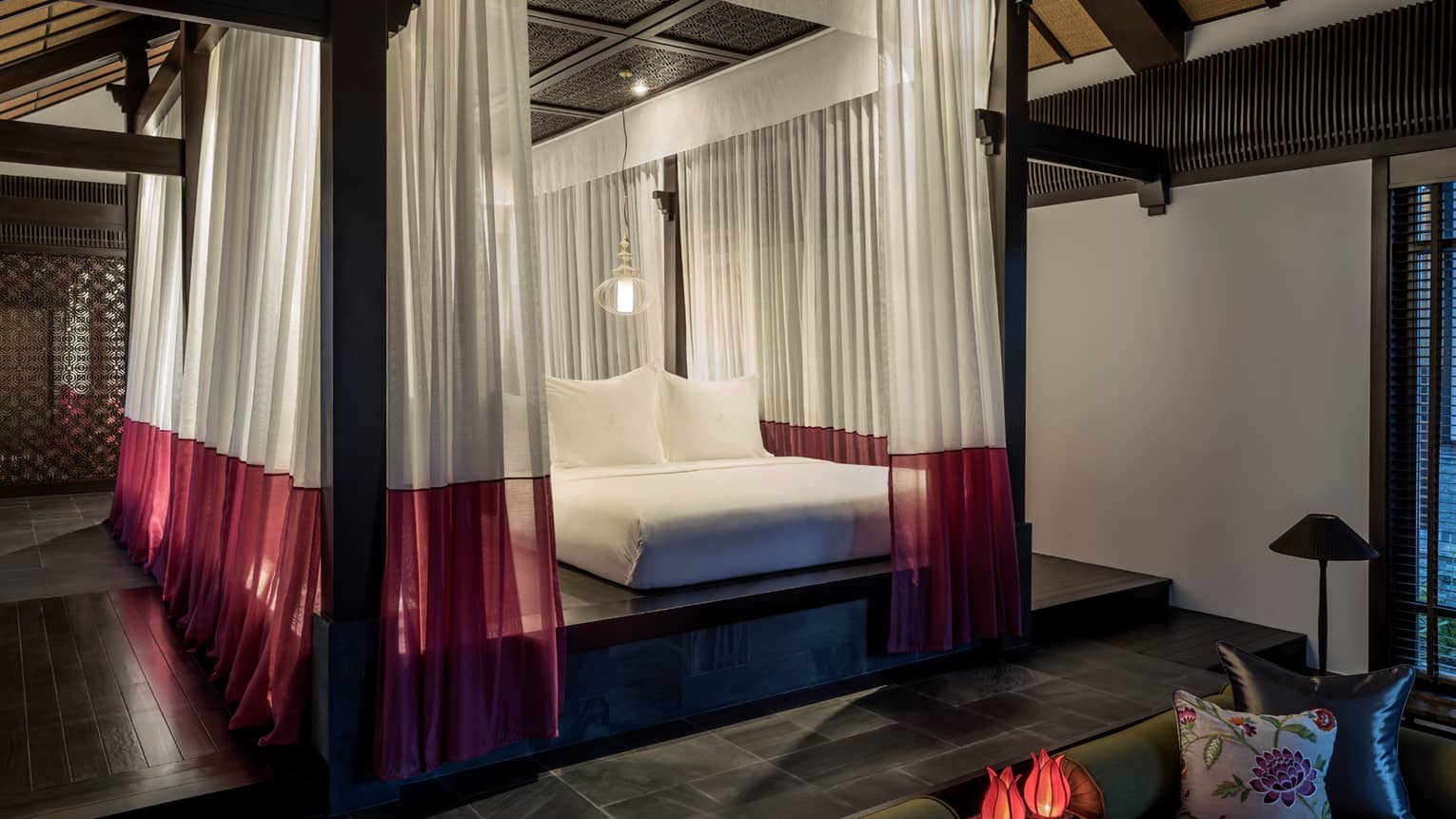 One-bedroom villa raised platform bed under sheer white-and-red drapes