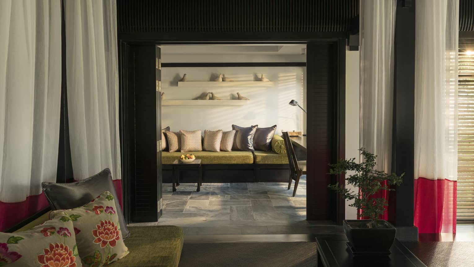 Cosy villa living room with warm lighting, featuring a sofa with colourful cushions, a small coffee table and decorative shelves with bird sculptures.