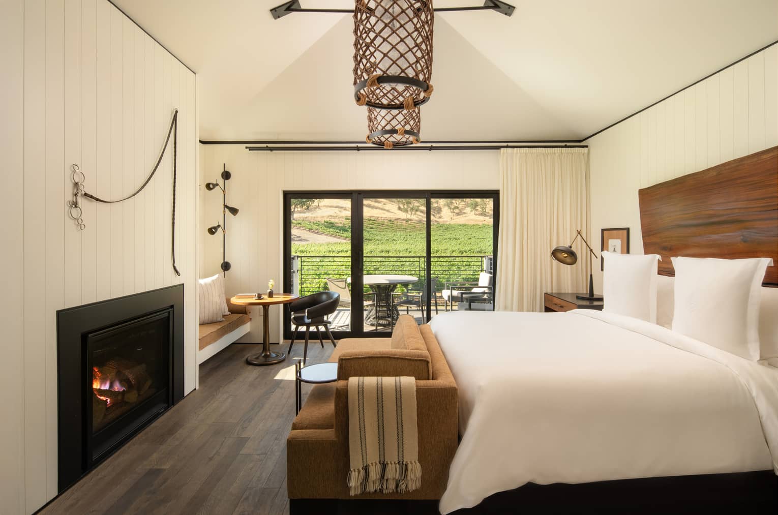 Contemporary bedroom of a resort suite, featuring king bed, fireplace, natural wood headboard, two hanging lights and walk-out terrace