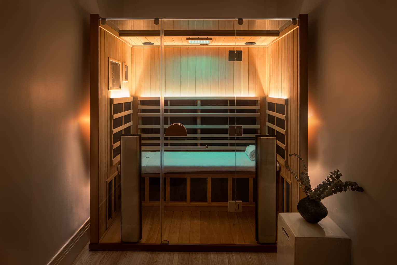 Wooden infrared sauna with lowlighting, side table with vase of eucalyptus 