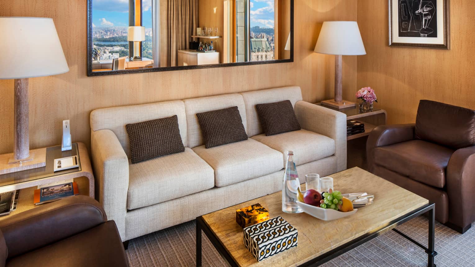 Central Park Suite white three-seat sofa with brown accent pillows under large mirror, table with fruit, water