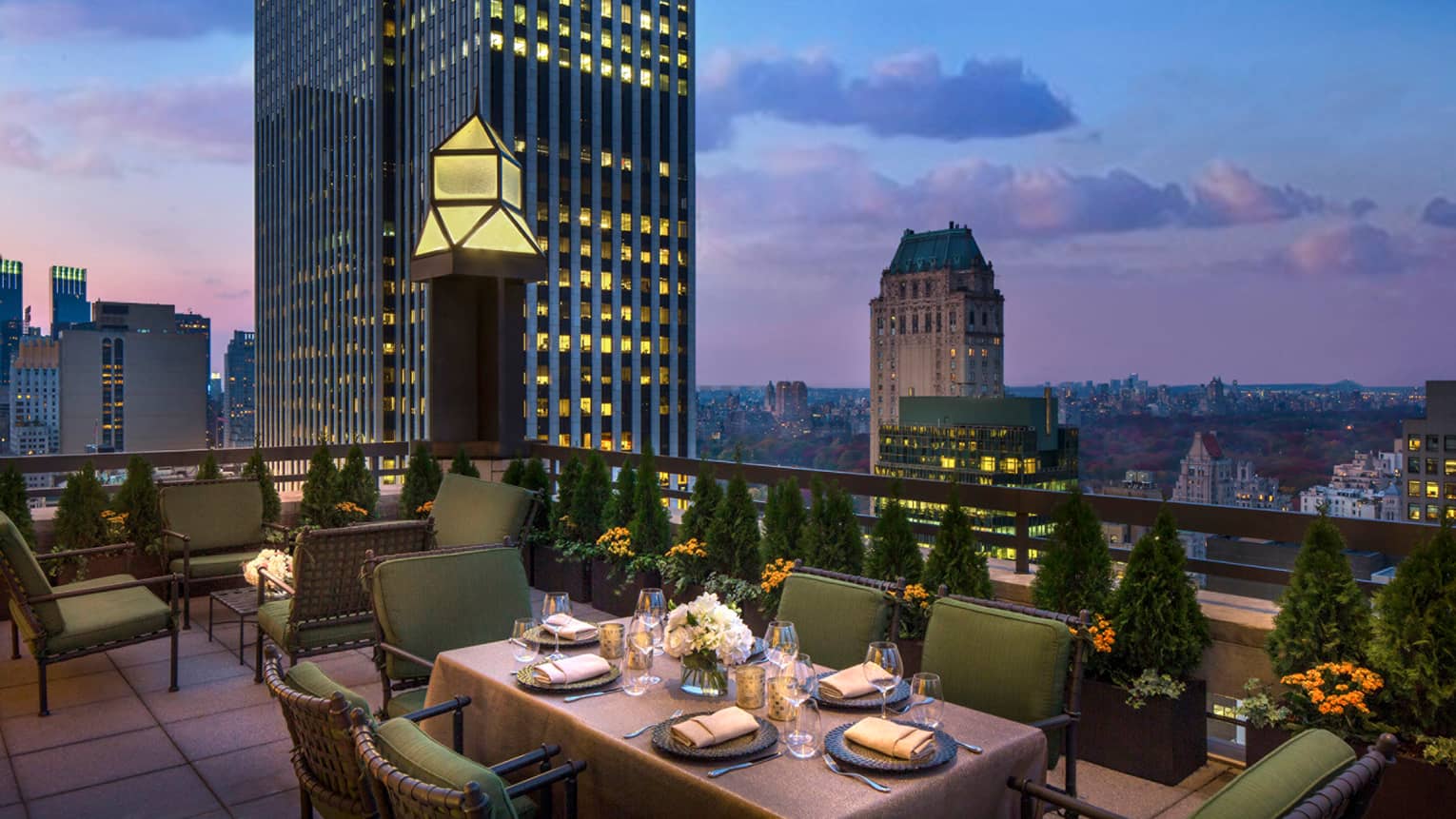 Private patio dining table with plush green cushions on chairs on rooftop terrace, city views at dusk