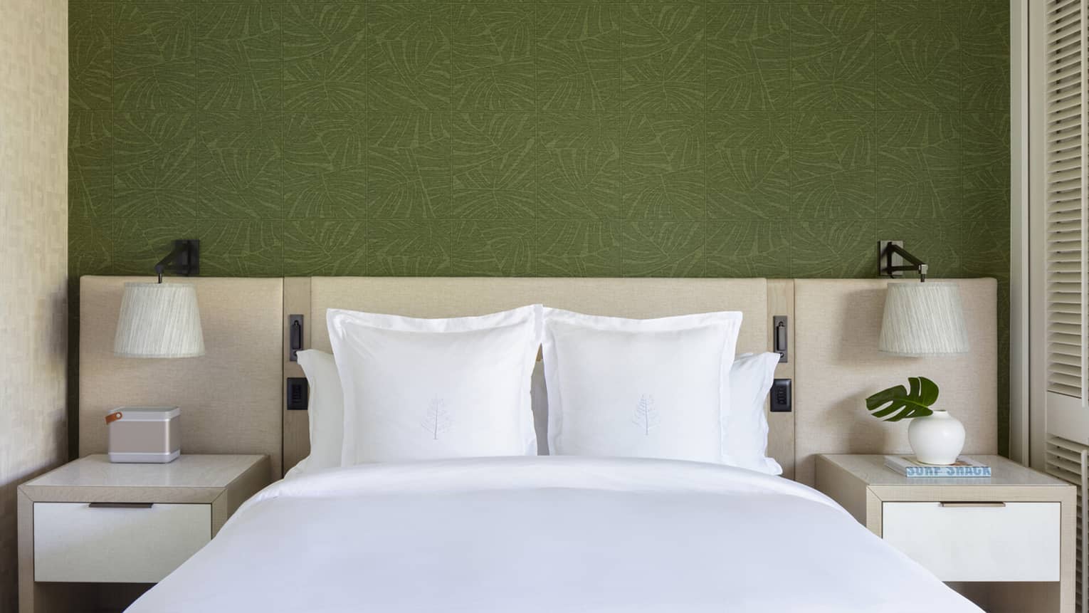 King bed with white sheets and Four Seasons logo on the pillows, set against green wallpaper