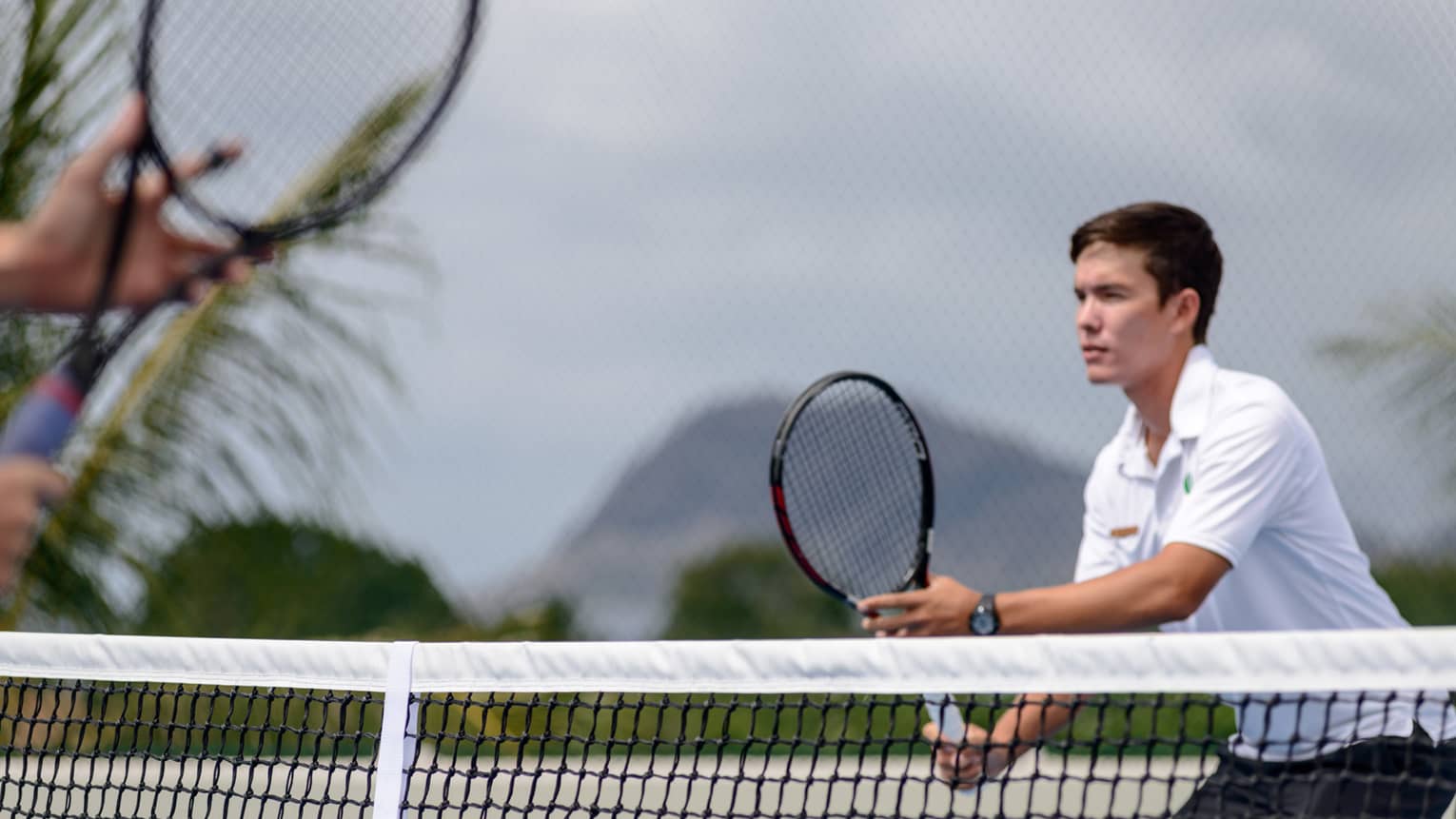 Man holds tennis racket near net in the Four Seasons Oahu Resort tennis centre