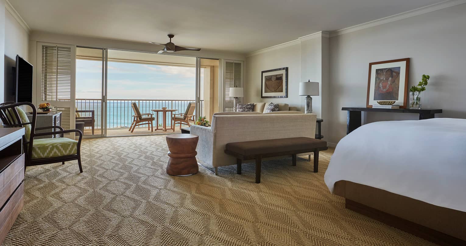 Oceanfront Junior Suite corner of bed behind living room, sofa facing open sliding patio doors