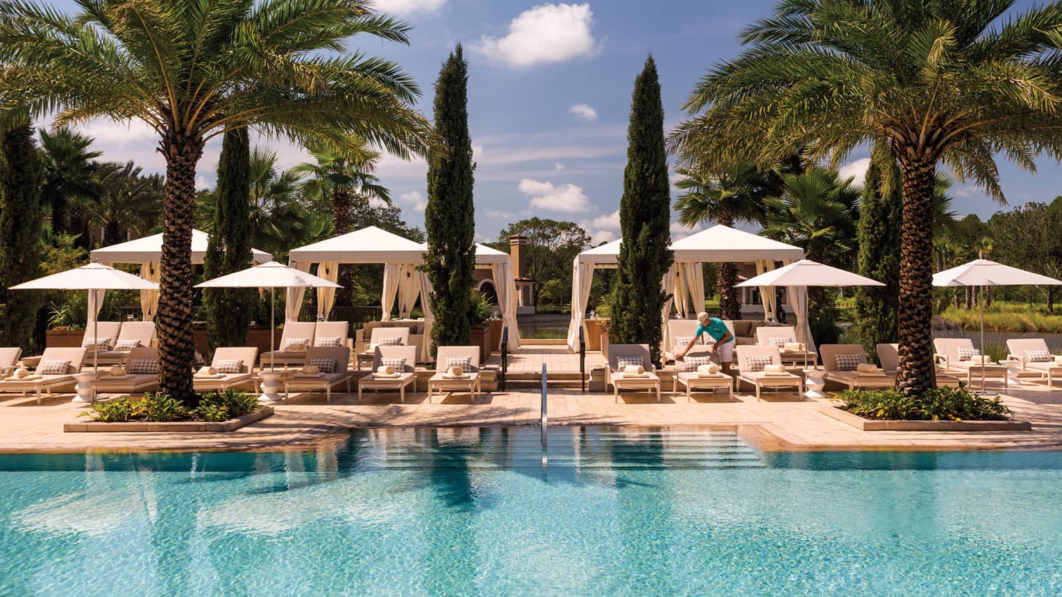 White cabanas, lounge chairs, palm trees along outdoor swimming pool deck