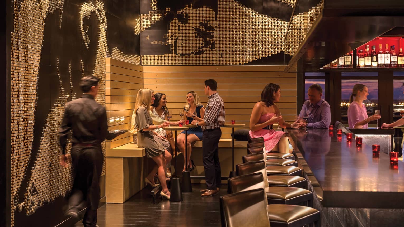 Group of friends socialize around Capa bar under mosaic tile wall