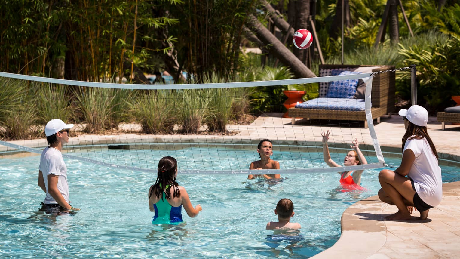 Kids play volleyball in small outdoor swimming pool with net