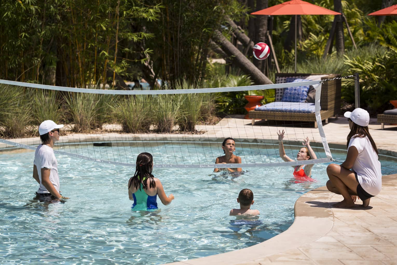 Kids play volleyball in small outdoor swimming pool with net