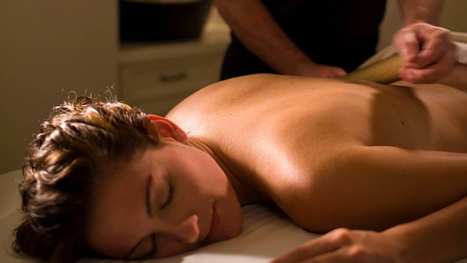 Woman lays on table as masseuse in black shirt massages her shoulders