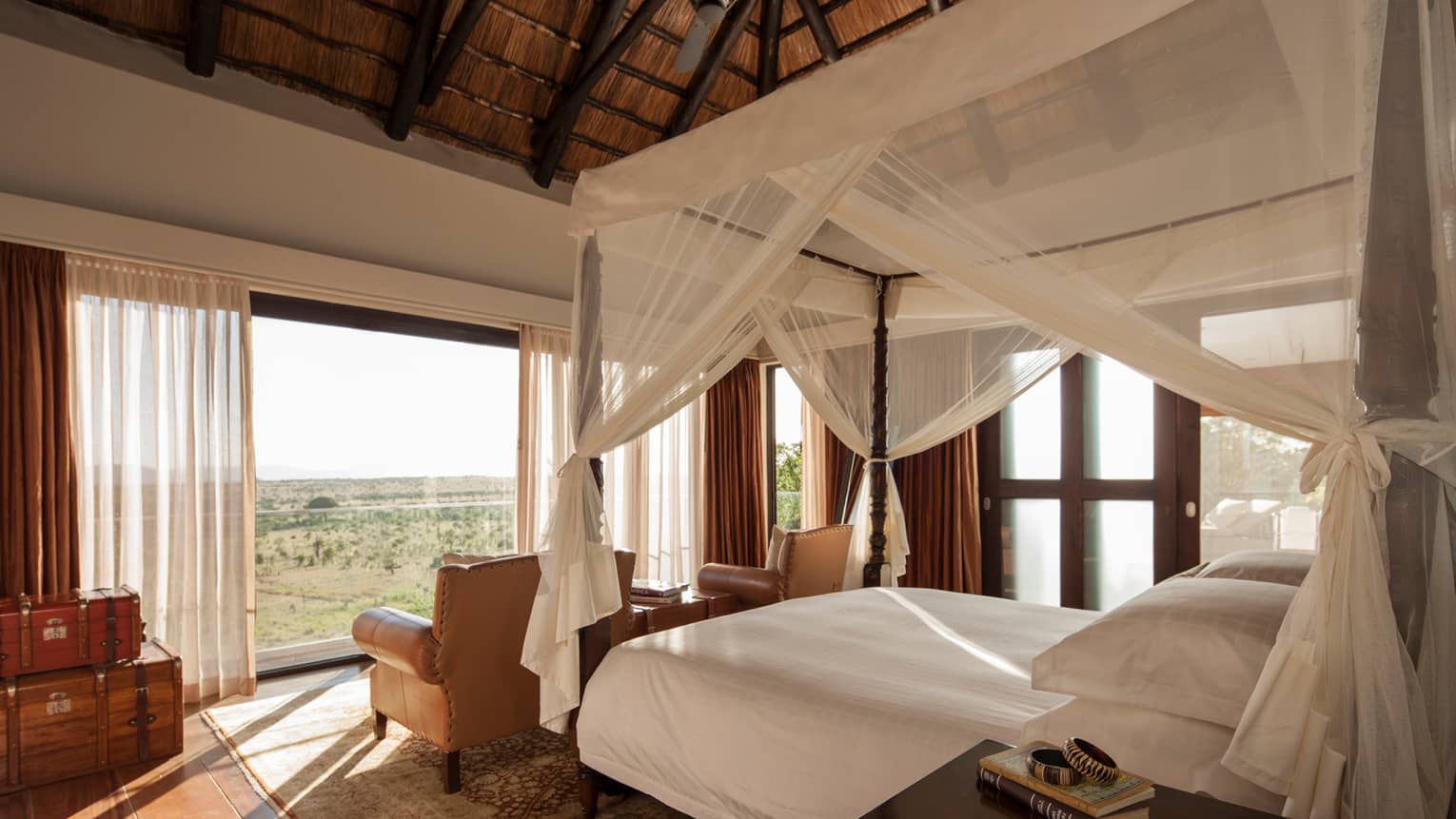Poster bed with sheer white canopy behind two leather armchairs facing open wall