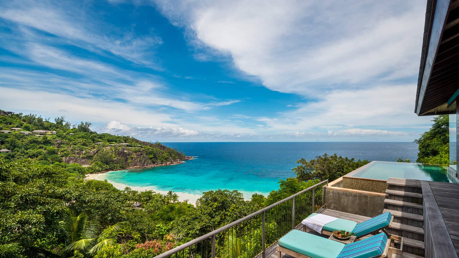 Blue lounge chairs on balcony overlooking lush mountain, beach, ocean, blue sky