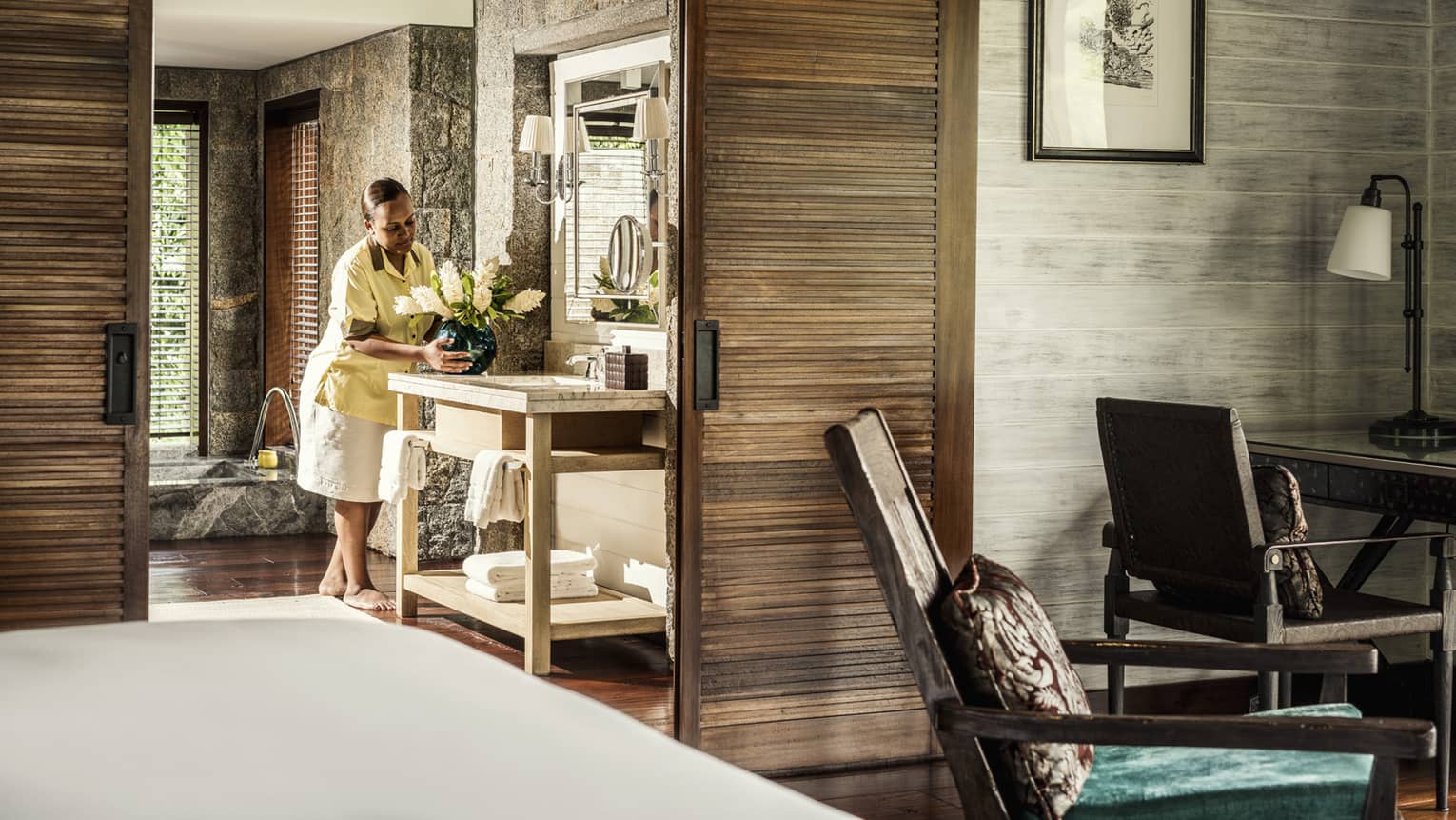 Villa butler places vase of flowers on vanity with towels in large bathroom