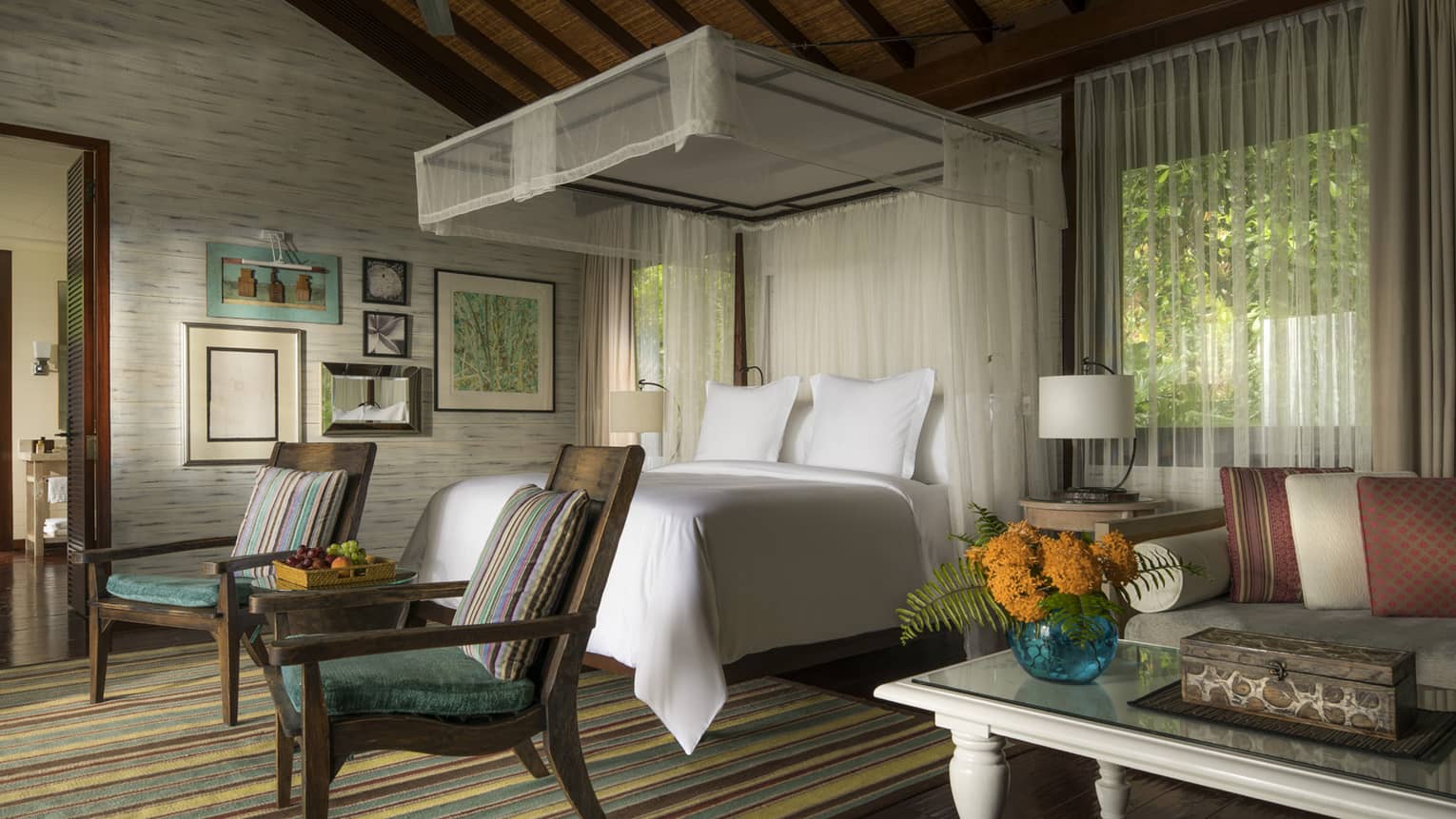 Suite with white canopied bed, two colourful striped chairs at foot, striped rug and sitting area