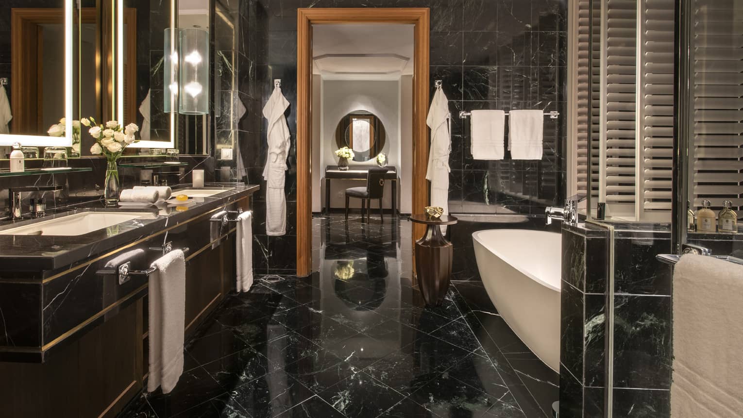 Bathroom with black marble floors and walls, double vanity, freestanding bathtub, glass shower and sitting area with soft lighting.