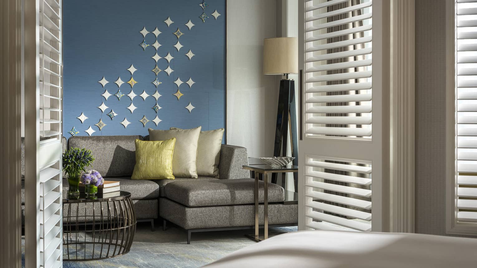 Gold pillows on grey sofa against blue wall with star-shaped Peranakan tile mural