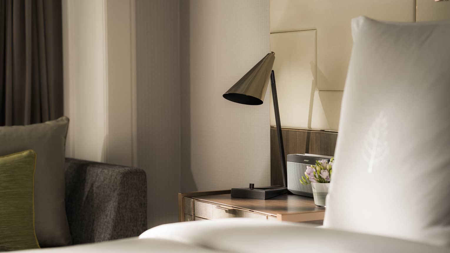 Modern silver lamp on nightstand beside alarm clock, bed 