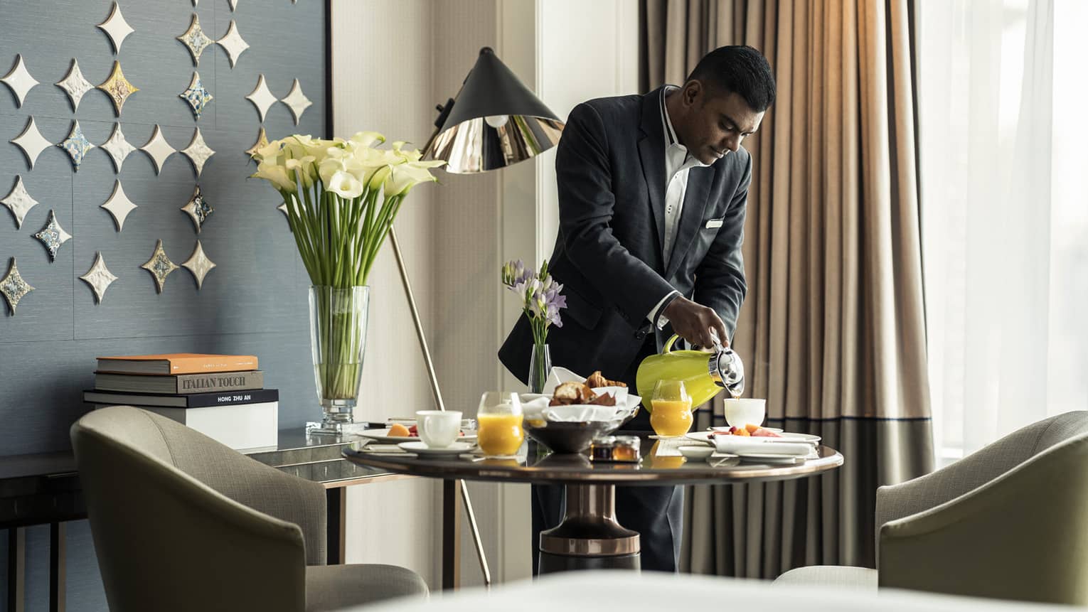 Hotel staff pours coffee from carafe into cup on brunch tray on in-room dining table