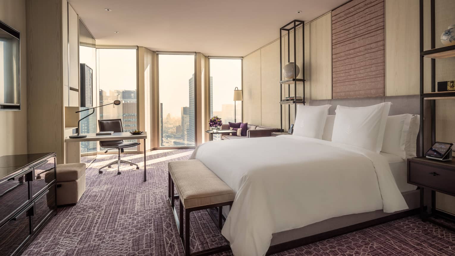 Hotel room bed with bench by work desk, chair near floor-to-ceiling windows