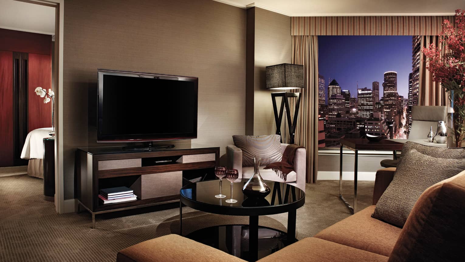 Club City Suite gold upholstered sofa, table with wine glasses, TV, bedroom door at night