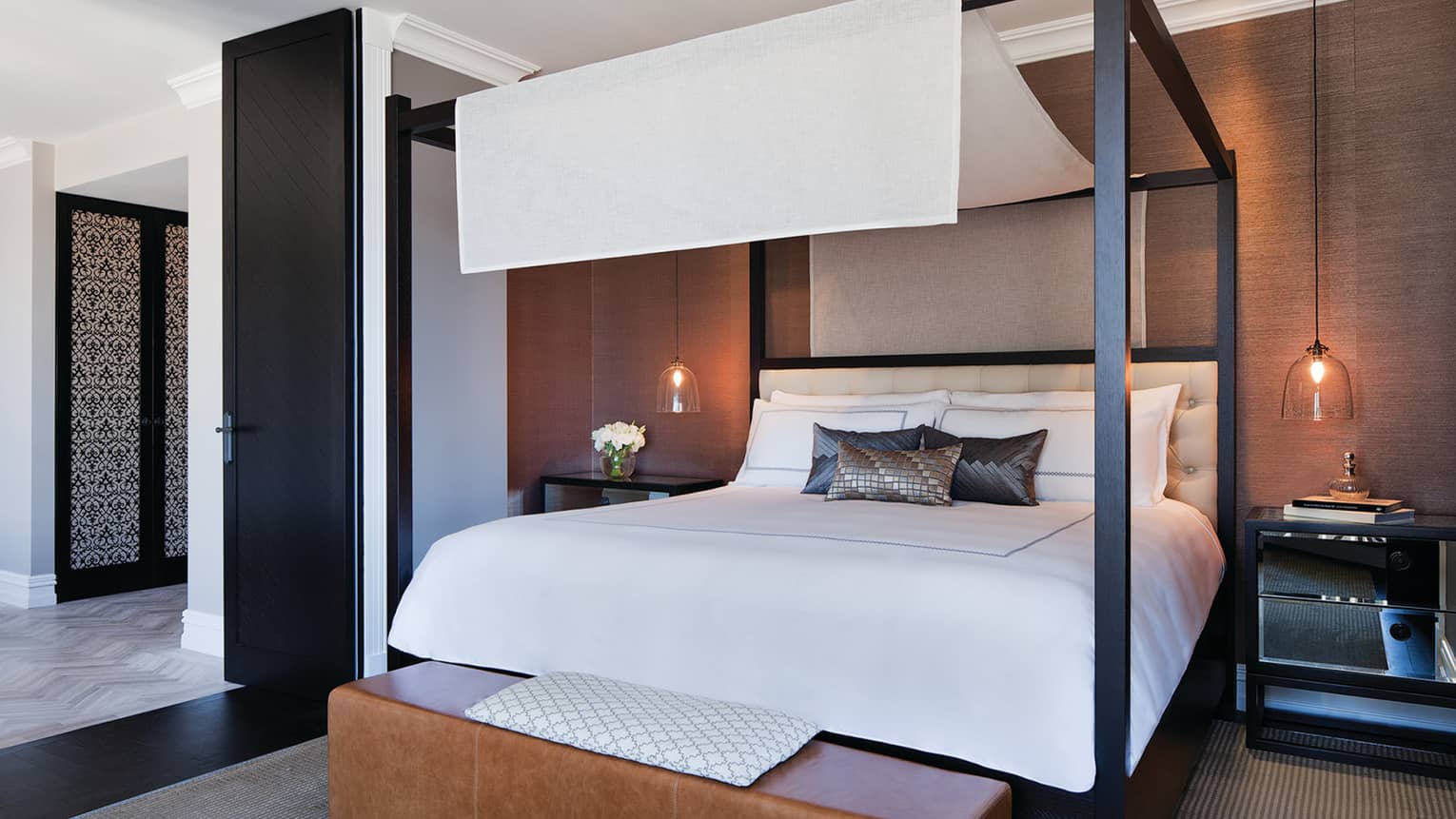 Poster bed with white linen canopy, silk accent pillows, brown leather bench at foot
