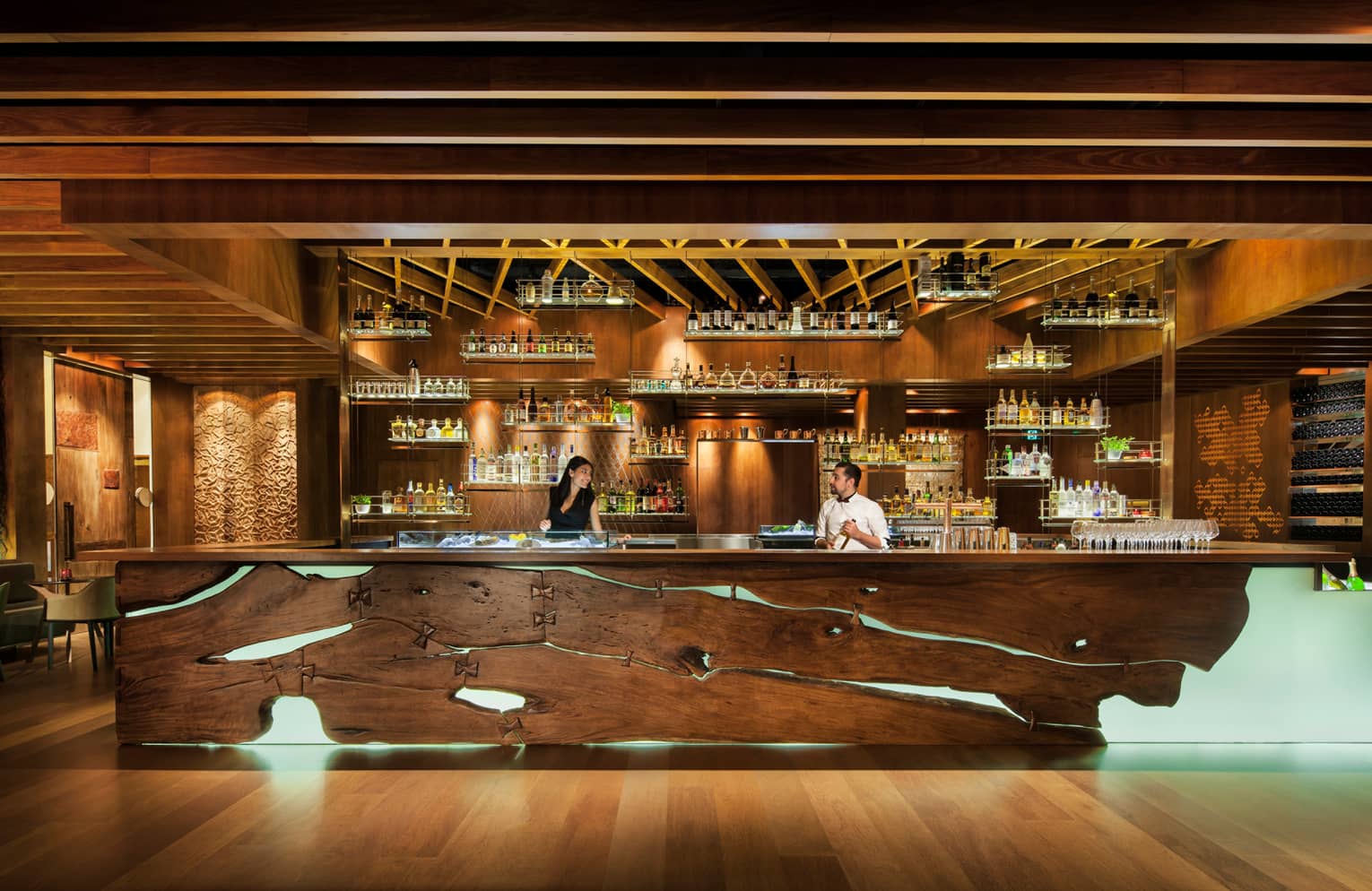 Two Grain bartenders behind rustic wood bar with lights, liquor bottles on shelf displays