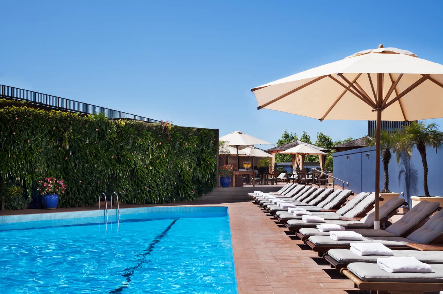 White lounge chairs lined up on deck under patio umbrella by blue outdoor swimming pool
