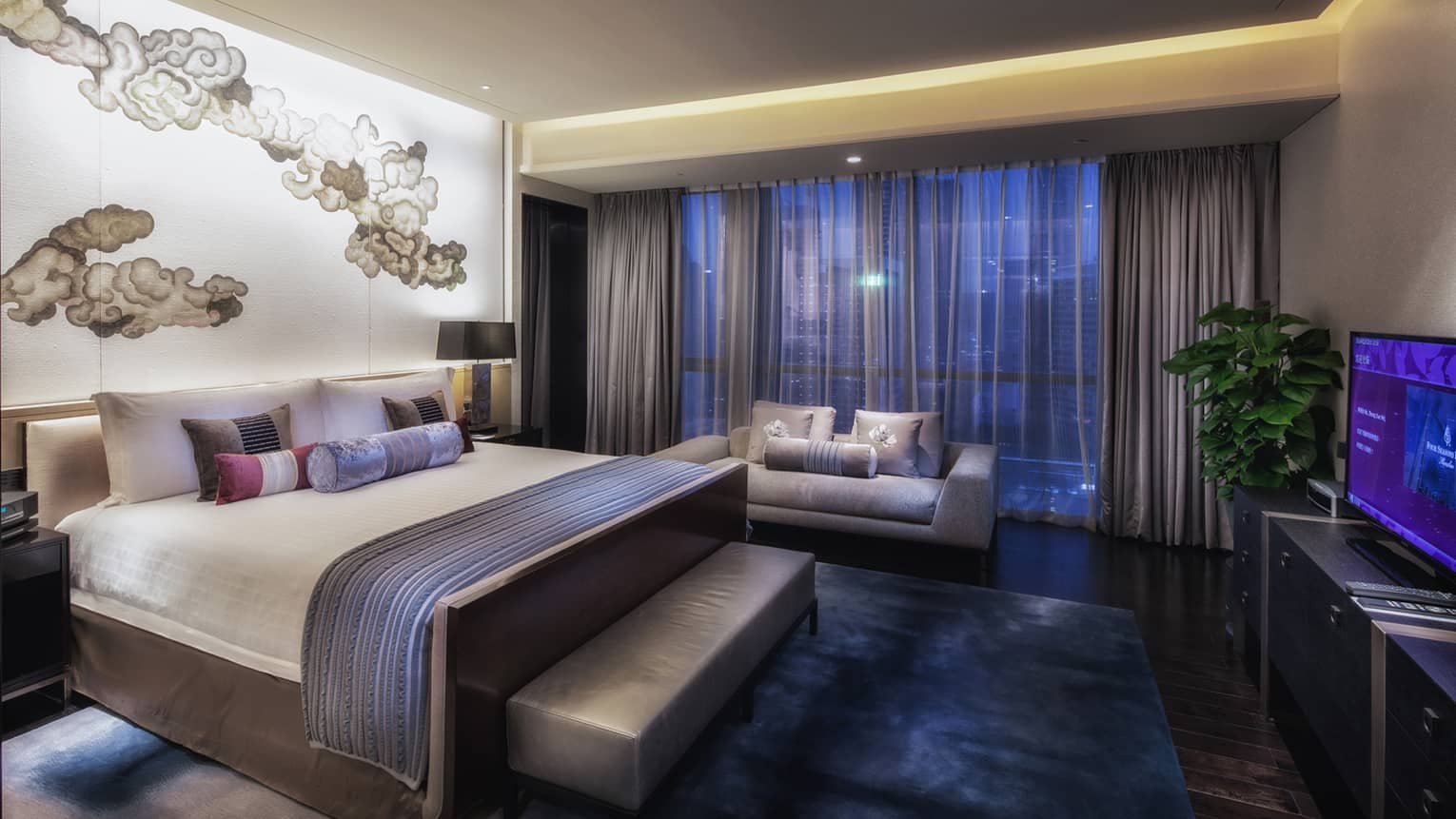Presidential Suite hotel bed and bench under lit-up accent wall across from TV, window