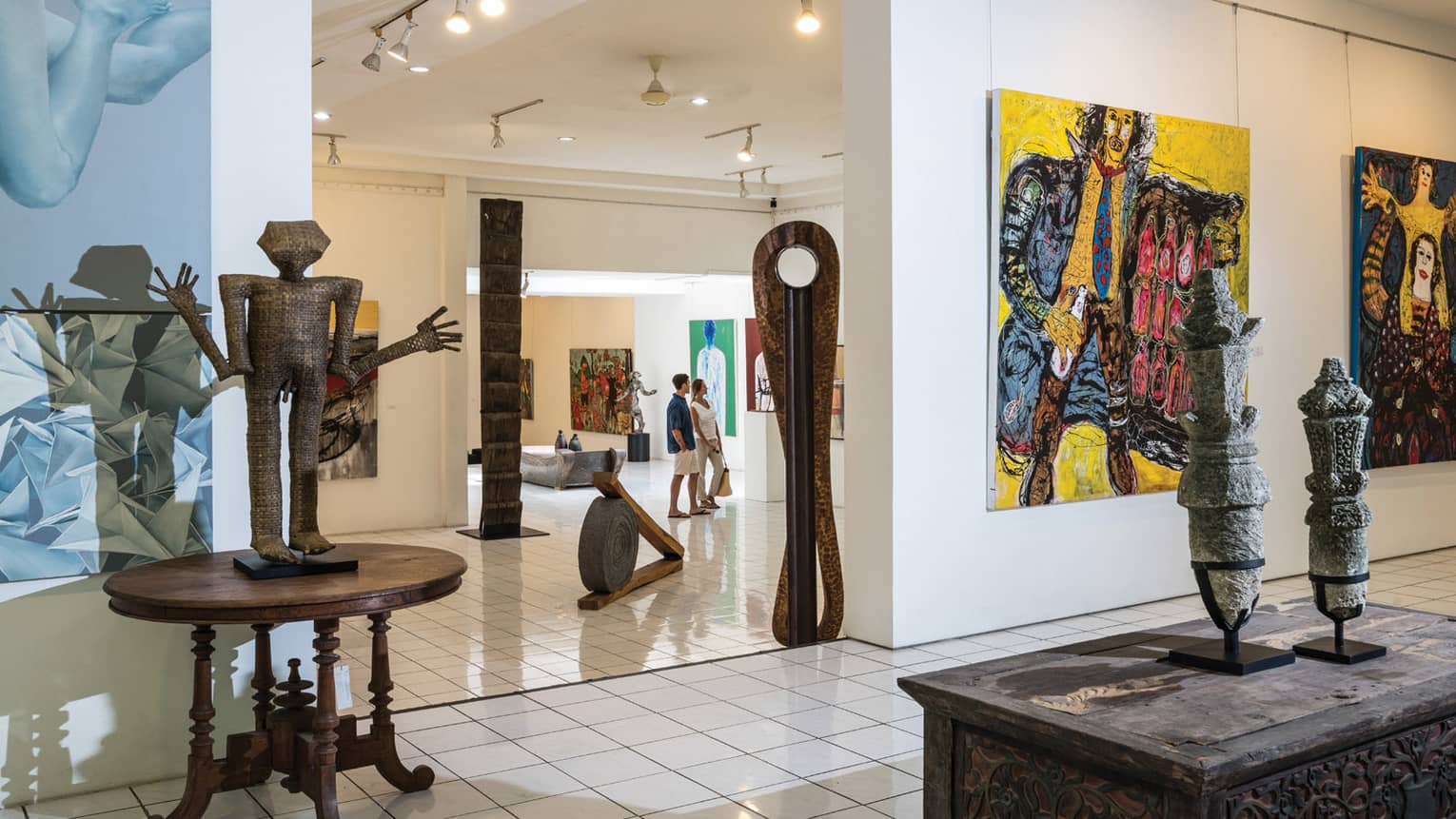 Couple walks through bright, modern art gallery with large sculptures, colourful paintings