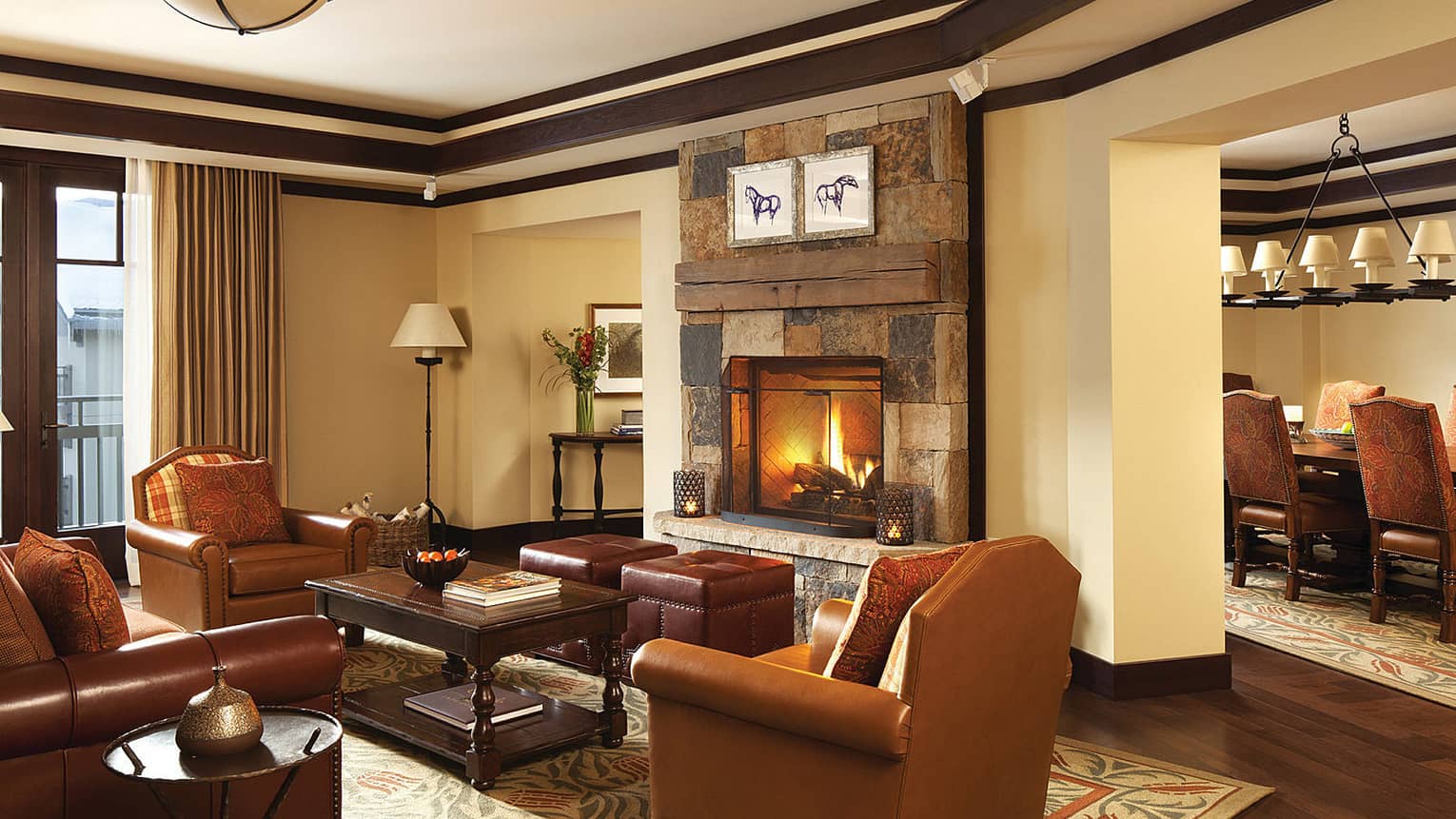 Brown leather sofa and armchairs in front of brick fireplace and fire, ranch-style dining table in view
