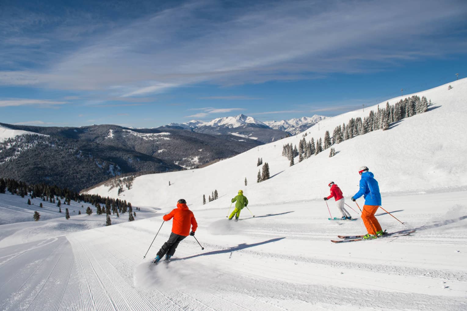 Four skiers in brightly coloured coats ski down mountain covered in snow