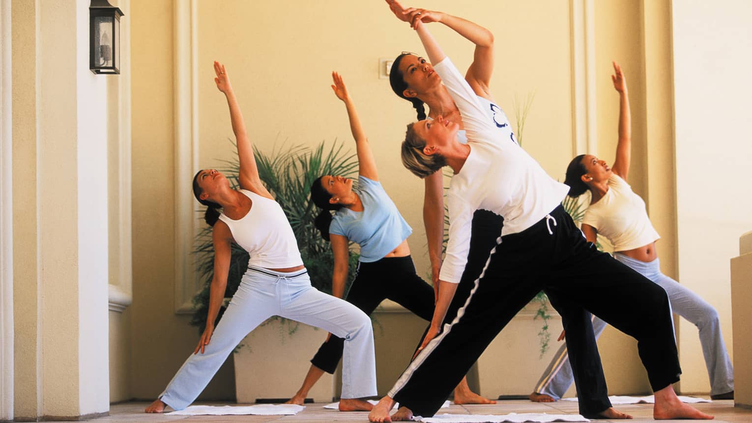Group fitness class, instructor helps woman stretch in yoga pose