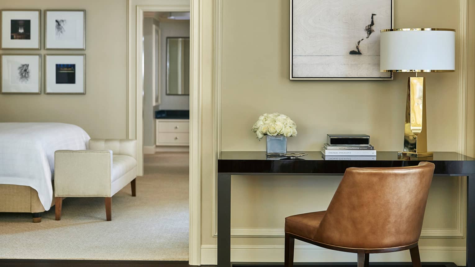 Modern brown leather office chair at black desk by doorway leading to bedroom, bed and bench visible
