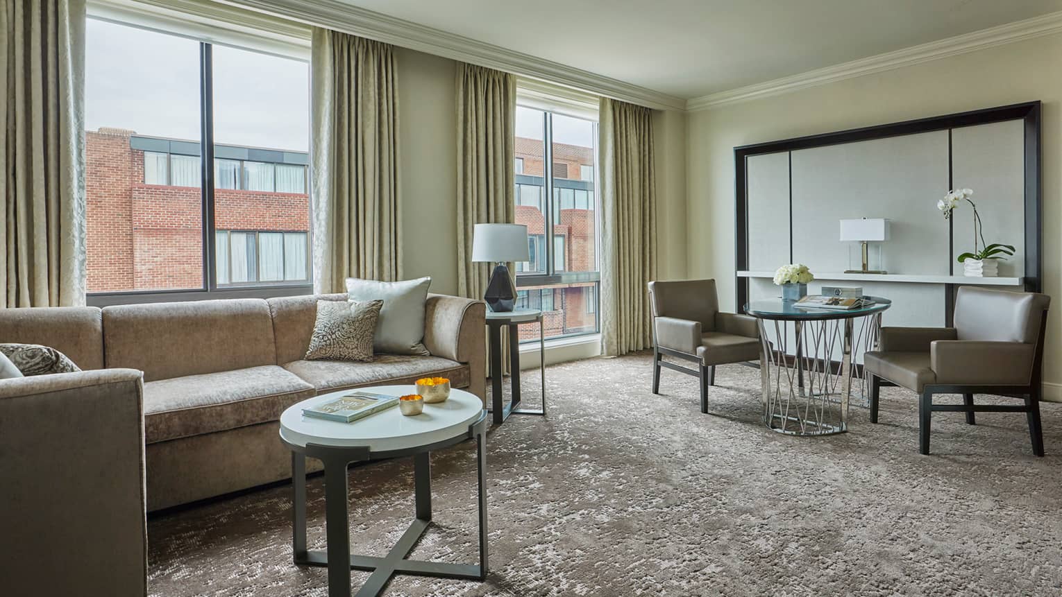 Premier Suite grey L-shaped sofa, small round white table, cafe-style dining table, large windows