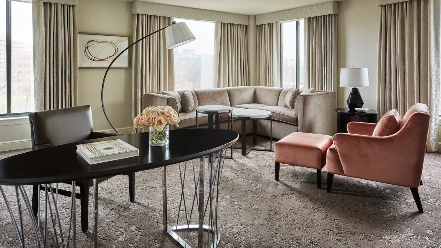 Capital Suite living room with long oval work desk in front of L-shaped sofa, pink armchair, corner windows