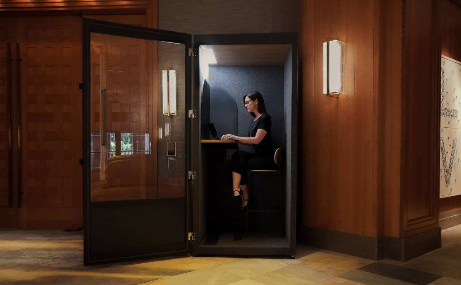 Woman sits in a glass-walled and sound-proofed virtual office room