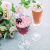 Two brightly colored cocktails with a fruit and floral garnish