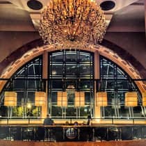 People dine in Nar Margot lounge under large glass chandelier and arched windows, row of lights 
