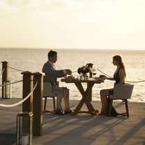 Couple dine at patio restaurant table by water at sunset