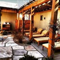 Stone patio with row of lounge chairs under pergola with vines