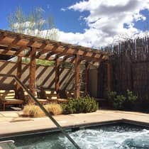 Outdoor spa tub steps and railing in front of patio, pergola and lounge chairs 