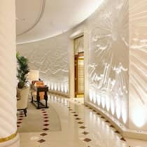 Luxurious hotel lobby with white walls, a large mural and illuminated curves above gleaming marble tile flooring