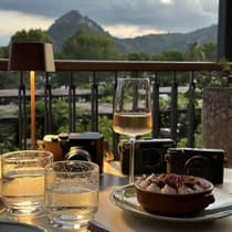 An outdoor dining table topped with a chocolate dessert and chilled white wine, overlooking a mountain view at sunset