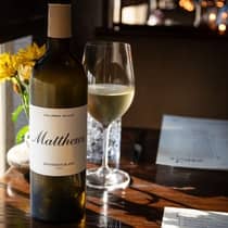 A bottle of sauvignon blanc wine in front of a filled wine glass on a wooden dining table next to two menus