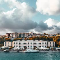 View from water to historic Istanbul Four Seasons hotel building under dramatic sky, clouds