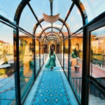 Woman wearing flowing dress walks down arched glass hallway