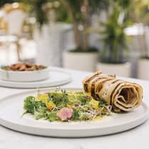 A grilled flatbread roll served alongside a vibrant salad of mixed greens, herbs and edible flowers, plated elegantly on a white ceramic dish