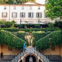 A man ascends a dual staircase to an outdoor terrace covered in lush greenery at the Four Seasons Hotel Milan